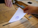 Une personne introduit son vote dans une urne.
